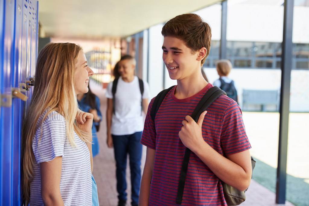 Two teenage friends talking in the school hallway.